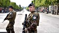 Zwei bewaffnete französische Soldaten stehen auf einer menschenleeren breiten Allee.