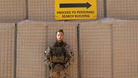 Ein Soldat lehnt unter einem Schild mit der Aufschrift "Proceed to Personnel search Building"