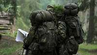 Zwei Soldaten mit Marschgepäck stehen in einem Wald und studieren eine Karte.