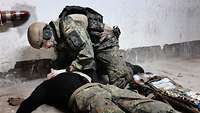 Ein Soldat kniet an einem simulierten Verletzten und behandelt ihn.