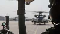 Links ist eine Visiereinrichtung und in der Mitte eine CH-53 zu sehen. Rechts ist ein Soldat der Bordbesatzung im Fokus