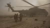 Vier Soldaten laufen mit einer Trage auf der ein Verletzter liegt zu einem Hubschrauber