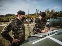 Zwei Soldaten mit Maske sehen auf eine Karte, die auf der Motorhabue liegt.