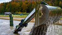 Aus einem Wasserbecken schauen der Turm und die Baggerschaufel eines Panzers. Aus der Schaufel läuft Wasser und Matsch