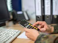 Ein Bundeswehrsoldat sitzt an einem Schreibtisch und rechnet mit einem Mobiltelefon