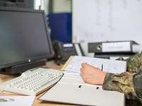 Ein Bundeswehrsoldat sitzt an einem Schreibtisch vor einem aufgeschlagenen Ordner