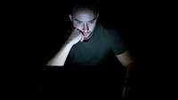 Ein Mann sitzt in einem dunklen Raum vor dem Computer