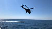 Ein Hubschrauber fliegt über ds Wasser.Im Wasser befindet sich ein Speedboot