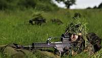 Ein Soldat liegt mit einem Gewehr im Anschlag auf der grünen Wiese in Stellung.