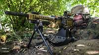 Ein Soldat mit Helm und Brille liegt auf dem Waldboden mit seinem Maschinengewehr in Stellung.