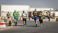 Eine Soldatin und drei Soldaten laufen in zivilen Sportklamotten in einem Bundeswehrcamp in Afghanistan.