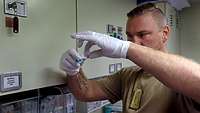 Ein Soldat steht in einem Raum mit verschiedenen Sanitätsmaterialien und zieht eine Spritze auf