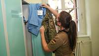 Eine Soldatin hat ihre Feldbluse ausgezogen und greift nach ihrer Arbeitskleidung