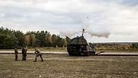 Soldaten vor einer Panzerhaubitze 2000 auf dem Truppenübungsplatz lösen mit einer langen Leine einen Schuss aus