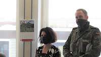 Eine Zivilistin und ein Soldat jeweils mit Gesichtsmaske stehen nebeneinander in einem Büroraum.
