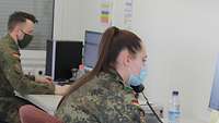 Eine Soldatin sitzt am Schreibtisch und telefoniert, im Hintergrund ein Kamerad am PC.