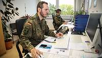 Zwei Soldaten sitzen nebeneinander im Büro an ihren Schreibtischen.