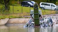 A tank enters a concrete pit filled with water. There are more cars in the background.