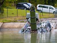 A tank enters a concrete pit filled with water. There are more cars in the background.