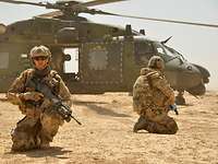 Soldaten knien in der Wüste vor dem Hubschrauber NH90.