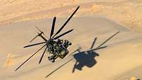 Ein Hubschrauber vom Typ CH-53 fliegt dicht über eine Wüstenlandschaft, ein Schatten entsteht