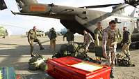 Mehrere Soldaten tragen Kisten und Gespäckstücke aus einem am Boden stehenden Hubschrauber vom Typ CH-53