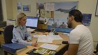 Hauptmann Christine Hausmann bespricht in ihrem Büro mit Mehdi Keskin seine Bewerbungsunterlagen. 