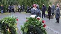 Ein Mann in Uniform steht vor Blumenkränzen