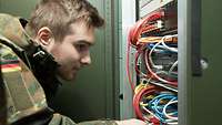 Ein Soldat schaut in eine Serverschrank mit vielen bunten Kabeln 