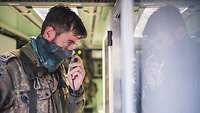 Ein Soldat spricht in ein Handfunkgerät und blickt dabei auf einen Schaltschrank.