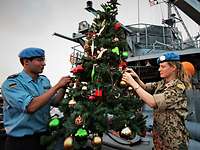 Zwei Marinesoldaten schmücken auf dem Deck eines kleinen Schiffes einen Weihnachtsbaum.
