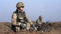 Zwei Soldaten in Wüstenflecktarn sitzen im Gelände und beobachten die Umgebung