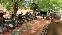Malische Soldaten mit Gewehren knien am Boden nebeneinander, ein deutscher Soldat beoabachten sie