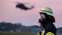 Ein Soldat mit Atemschutzmaske. Im Hintergrund fliegt am Himmel eine CH-53