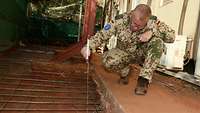 Ein Soldat kniet mit einem Metermaß in der Hand neben einem Loch und vermisst die Tiefe