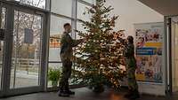 Zwei Soldaten schmücken einen Weihnachtsbaum.