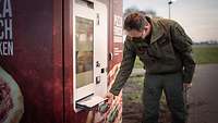 Männliche Person in Uniform entnimmt einem Automaten eine Pappschachtel