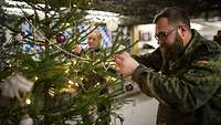 Eine Soldatin und ein Soldat hängen Weihnachtsschmuck an einen Tannenbaum