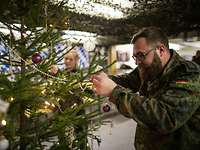 Eine Soldatin und ein Soldat hängen Weihnachtsschmuck an einen Tannenbaum