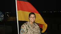 Eine lachende Soldatin steht bei Dunkelheit vor einer Deutschlandflagge