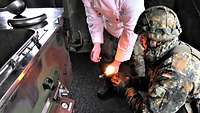 Ein Soldat im Kampfanzug und Helm kniet vor dem Petroleumbrenner mit einem brennenden Docht in der Hand.