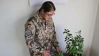 Eine Soldatin steht vor einem Tisch mit zwei Topfpflanzen und gießt diese
