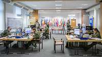 Several soldiers are sitting at their workplaces separated by Plexiglas screens.