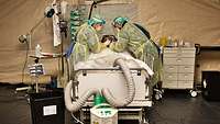 Two soldiers in protective clothing treat an intensive care patient.