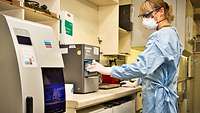 A woman in protective clothing operates a laboratory analysis device