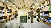 Shelves full of materiel in a tent. Four military personnel are busy putting further materiel in the right place.