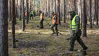 Soldaten mit Warnwesten und Mundschutz laufen in einer Reihe durch einen Wald.