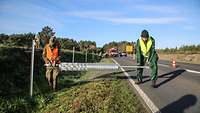 Ein Soldat und ein Arbeiter in grünen Arbeitssachen entrollen gemeinsam den Schutzzaun.