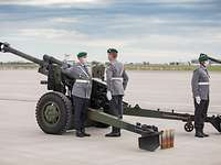 Drei Soldaten in Heeresuniform stehen in Position an einer Feldhaubitze.