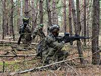 Drei Soldaten kämpfen mit Sturmgewehren im Wald.